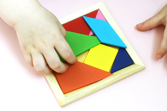 Children&rsquo;s hands solving a colorful wooden tangram puzzle on a pink background, encouraging logic and imagination. Perfect for educational resources, early learning ads, parenting sites, and games.