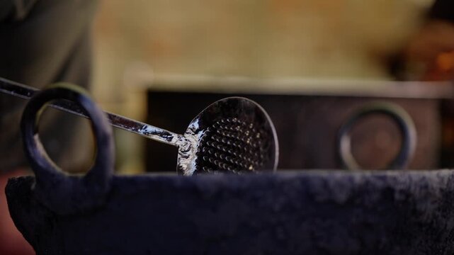 Fried samosa lifted on a metal skimmer with oil dripping in mid air above black iron kadai, shallow depth of field with warm blurred background