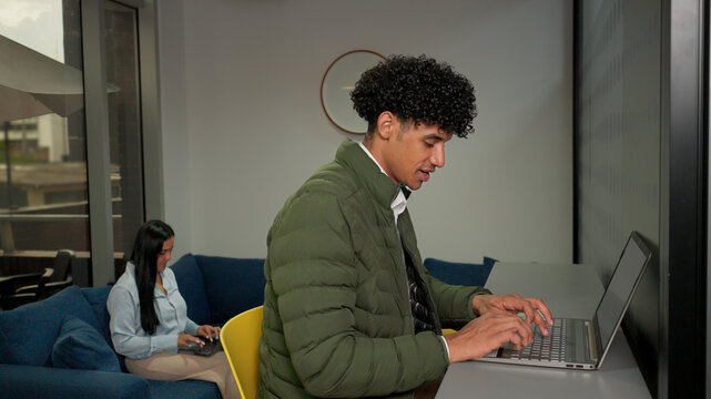 Latin Man Working On A Laptop From A Shared Counter In A Flexible Office