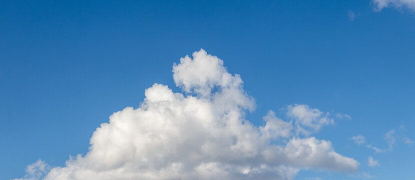 Panorama of a bright blue sky with a large white fluffy cumulus cloud in the center of the frame and small clouds with free space for text on a clear sunny day