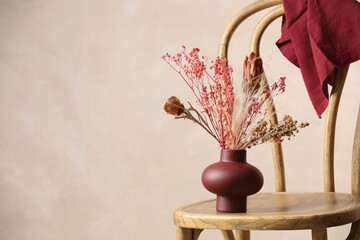 Beautiful dried plants in vase on wooden chair against beige background. Space for text