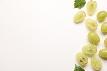 Fototapeta premium Fresh ripe grapes and green leaves on white background, flat lay. Space for text