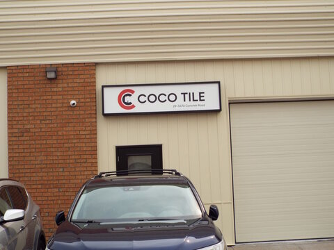 Gloucester, Ontario, Canada &ndash; July 31, 2026: A lighted business sign for "Coco Tile" is mounted on the exterior wall of a commercial building above parked cars at 5470 Canotek Rd Unit 29.