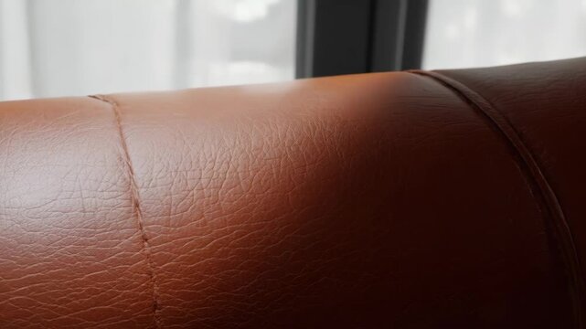 Detail of a cognac-colored leather surface with visible stitching and a textured grain on upholstered furniture.
