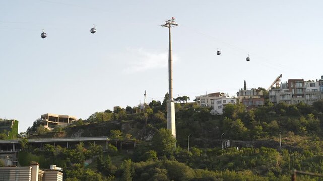 Modern air cable car cabins passing by over hillside in Tbilisi, Georgia, public transportation service, gondolas at aerial tramway moving along tower over urban city, touristic sightseeing landmark.