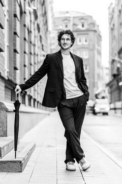 Street style photography. Young sexy handsome attractive looking fit stylish man in a black suit posing outdoors. Black and white portrait, casual clothes. City landscape on background