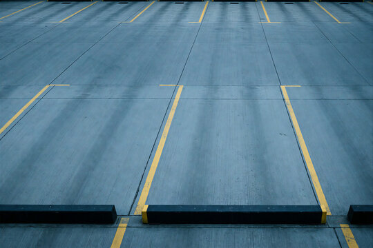 Empty concrete parking lot with yellow lines and wheel stops