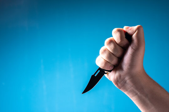 Hand with a combat knife on a blue background. Murder.
