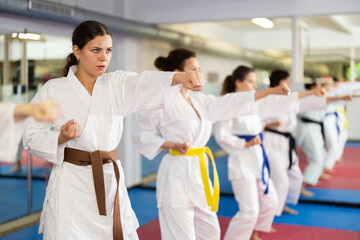 Women athletes learn practice of kata karate punches, hone fighting skills by repeated repetition. In gym, master coach during karate kata lesson with team students group, kata formation position. © JackF
