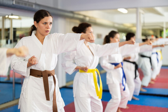 Women athletes learn practice of kata karate punches, hone fighting skills by repeated repetition. In gym, master coach during karate kata lesson with team students group, kata formation position.