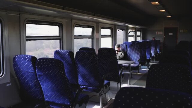 Passenger uses smartphone inside nearly empty train carriage during off-peak railway journey with fewer crowds more personal space and quiet shoulder season travel.