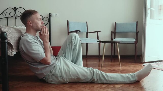 Man with anxiety sits on floor at home alone, coping with stress and uncertainty while thinking through difficult decision and trying to regain emotional control.