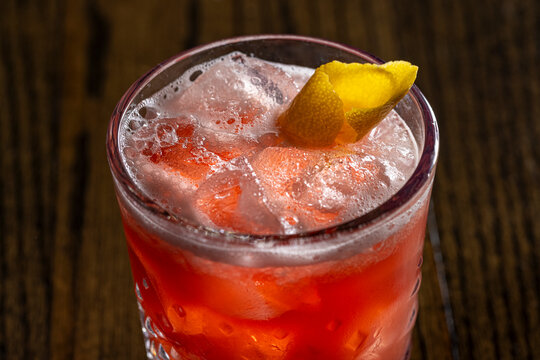 Frothy pink cocktail with lemon on ice