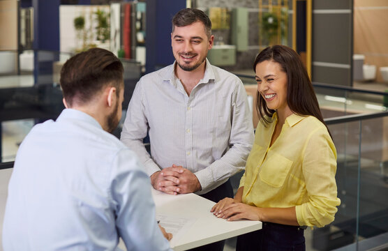 Couple customer cliemts interacting with saler, supervisor in office show room listening and smiling, discussing decor ideas, demonstrating goods, showing displays, positive client relationships