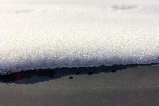 Sparkling snow layer melting on a dark surface in sunlight