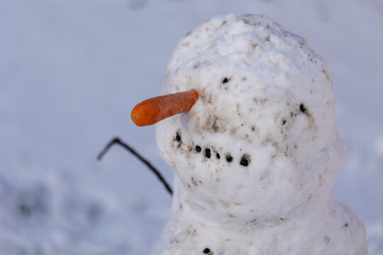 Close up of a handmade snowman head with carrot nose in snow