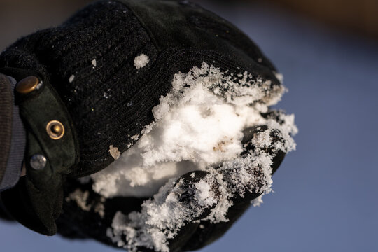 Person holding fresh white snow in black winter glove