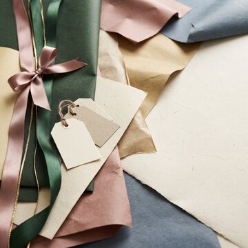 A beautifully wrapped gift tied with satin ribbons and accompanied by blank gift tags, set against a backdrop of decorative wrapping papers in muted tones, perfect for any occasion.