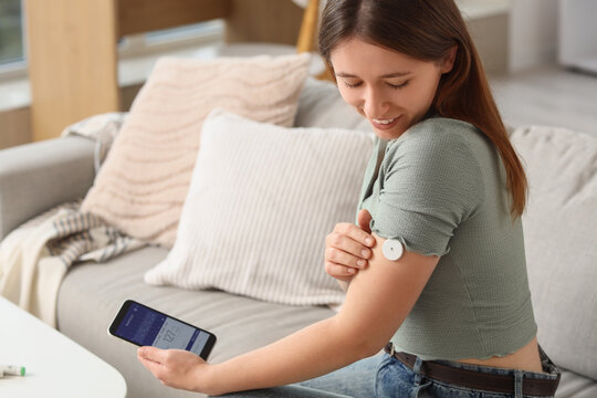 Diabetes management and glucose monitoring, woman using a continuous glucose monitor sensor and smartphone app at home for health tracking