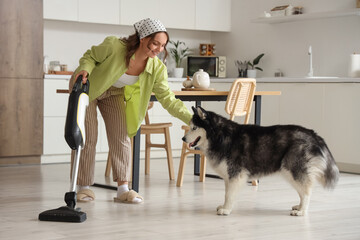 House cleaning and pet care, woman using a cordless vacuum cleaner while petting her husky dog in a modern kitchen for a domestic lifestyle © Pixel-Shot