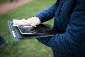 Person in a blue jacket wiping a tablet screen with a wipe outdoors © janvaneyck