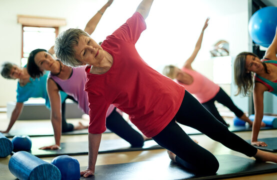 Active, senior and woman in pilates class for wellness, mobility exercise and healthy body. Side plank, elderly and female person in gym studio for workout, fitness training and physical wellbeing.