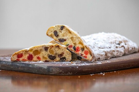 Christstollen, traditional German Christmas fruit bread dusted with powdered sugar and cut into slices, showing the dense crumb studded with candied cherries, candied fruit, raisins and nuts.