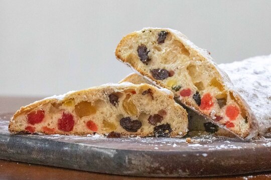 Christstollen, traditional German Christmas fruit bread dusted with powdered sugar and cut into slices, showing the dense crumb studded with candied cherries, candied fruit, raisins and nuts.