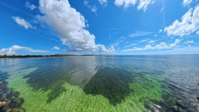 Camera pans over clear tropical ocean water beneath dramatic clouds in Key West.