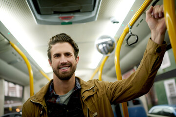 Portrait, bus and man with smile, travel and public transportation with city service. Face, morning commute or passenger with handrail, safety or relax with urban journey, ride destination or trip © peopleimages.com