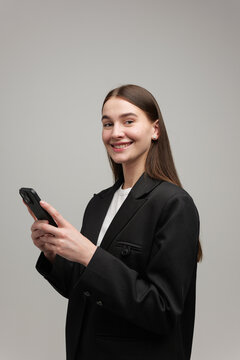 Young woman in a stylish black blazer smiling while using her smartphone indoors