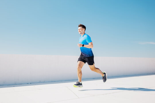 Joyful man jogging under a clear blue sky in a modern urban setting