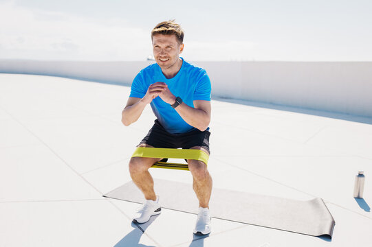 Fitness enthusiast performs squats with a resistance band on a sunny rooftop terrace