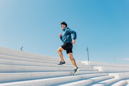 Runner sprints up bright white stairs under a clear blue sky during morning exercise