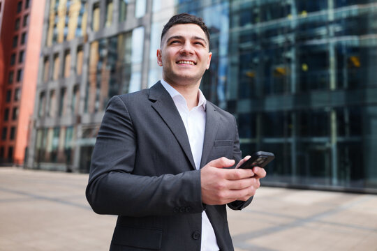 Business professional smiles while checking smartphone outside modern urban building