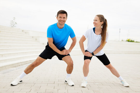 Fitness enthusiasts warm up together outdoors with smiles under an overcast sky