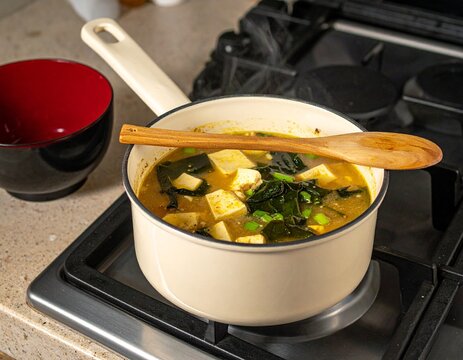 Japanese miso soup with tofu and wakame seaweed cooking in a pot on a gas stove.