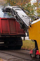 Asphalt milling machine loading old pavement into dump truck, road works. Urban infrastructure, modernization, asphalt recycling  © Alena Malinouskaya