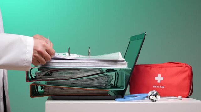 Doctor working with patient files, organizing important documents, and utilizing a laptop for modern healthcare data management, alongside a first aid kit and stethoscope