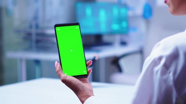 side angle shows a doctor holding a vertical smartphone green screen while a colleague opens the glass door, creating a clean mobile healthcare mockup.
