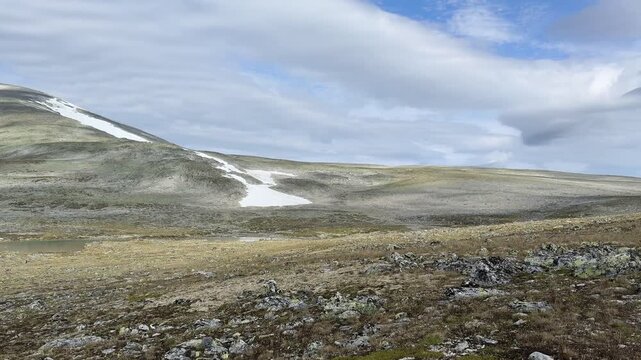 Snow patches on a mountain slope with distant hikers