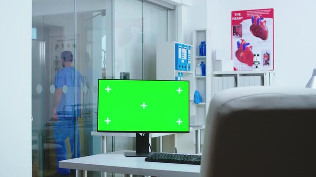 Green screen monitor on a medical office desk as a healthcare worker moves into the elevator, combining clinical workplace context with mockup space.