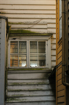 Weathered white wooden boards with moss stains around an old mullioned window in the Bryggen quarter of Bergen.