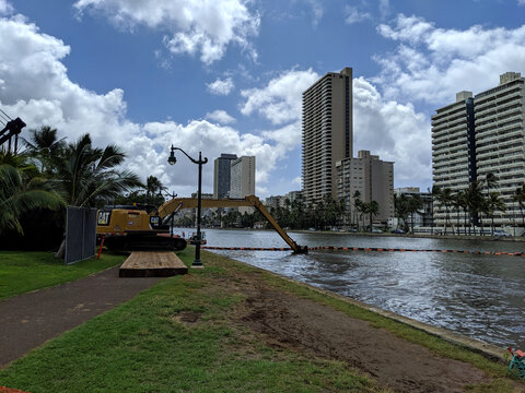 Construction work along Ala Wai on Oahu with heavy machinery near the water on a sunny day