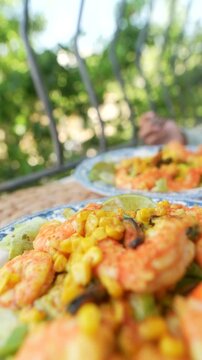 Fork-to-mouth bite of shrimp salad with fork pressing leafy greens to lips on blue patterned plate in sunlit garden balcony setting showcasing creamy avocado and crisp lettuce