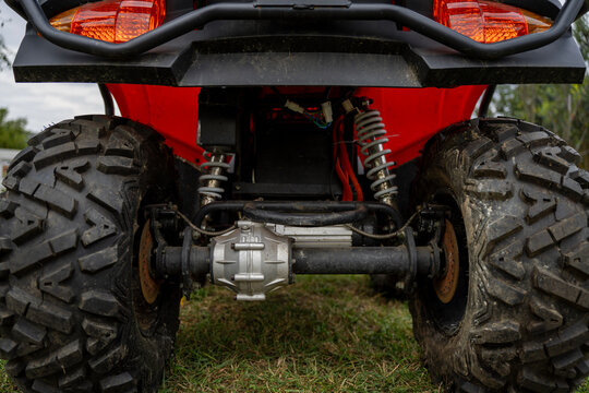 Rear view of a red all-terrain vehicle exposes its differential, drive axle, coilover shocks, wiring, taillights and mud-terrain tires outdoors.