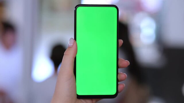 Hand holds smartphone with green screen. Background blurred. Three keyframes show same scene. Human hand visible
