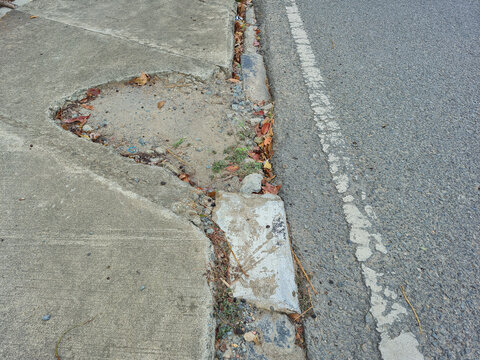 ​Damaged concrete sidewalk with cracked pavement eroded curb and broken asphalt road infrastructure