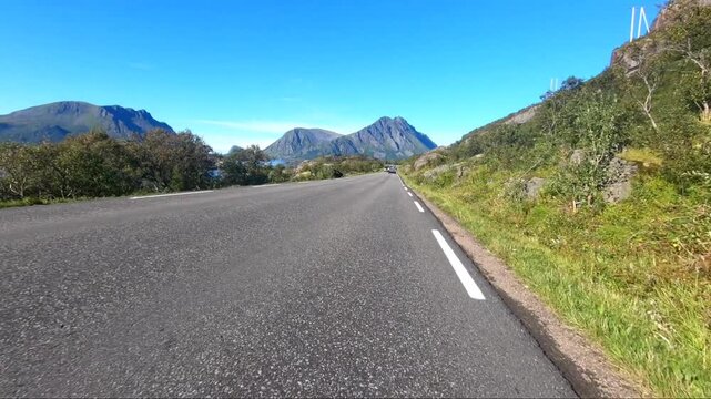 An open road through a picturesque mountain landscape with a clear blue sky, the sea can be seen, E 10, Lofoten, Nordland, Norwgn