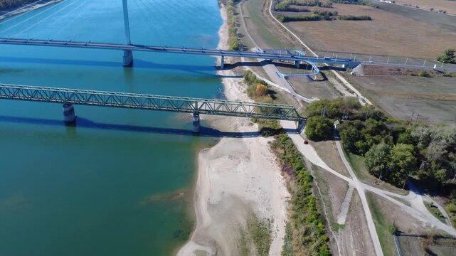 Aerial view approaching two bridges crossing a wide river next to a sandy bank
